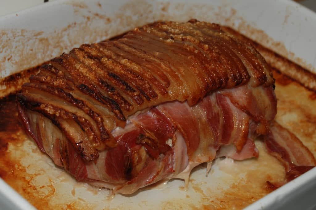 Flæskesteg i svøb Man tager en flæskesteg, pakker den ind i bacon, og putter den så i ovnen...